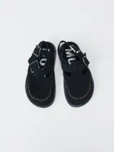 Slipper tipo guillermina confeccionada en gamuza negra, con plataforma de goma, doble hebilla ajustable y detalle de pespunte en contraste en el borde inferior.