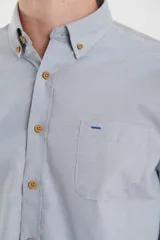 Camisa de vestir blanca de manga larga, con cuello abotonado, bolsillo frontal y botones en tono madera.