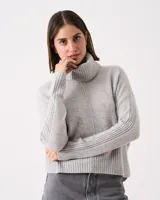 Sweater gris claro de tejido de punto con cuello alto acanalado. Presenta un diseño vertical en el centro delantero y trasero, punto diferencial en las mangas, ruedo con tajo lateral y puños acanalados.