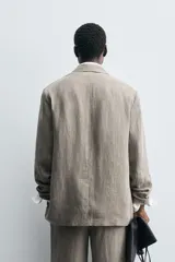 Blazer de corte relajado confeccionado en lino con efecto lavado. Presenta cuello con solapas de pico, cierre frontal de un botón, manga larga y bolsillos con solapa en la parte frontal.