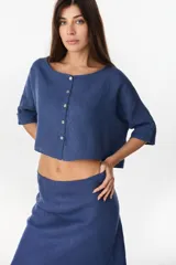 Camisa de lino azul marino, de corte crop y holgado, con cuello redondo, botonadura frontal y mangas amplias con vuelta.
