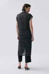 Kimono tejido de punto en color crudo con sutil brillo de lurex. Presenta un diseño sin mangas, corte largo y cierre frontal mediante dos lazos finos. El tejido tiene una textura acanalada vertical.