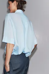 Camisa de color mostaza, con cuello solapa, manga corta y bajo recto. Cierre frontal con botones.