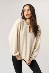 Sweatshirt de tejido suave color beige, con cuello en V con ribete texturizado, hombros caídos y mangas largas amplias con puños acanalados.
