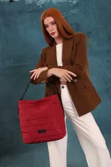 Cartera tipo tote de diseño capitoneado con patrón geométrico triangular. Presenta un acabado acolchado, asa de mano resistente y cierre superior. Incluye una etiqueta decorativa en la parte inferior frontal.