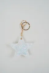 Llavero metálico dorado con dije en forma de estrella cubierto de glitter blanco y argolla con cierre de mosquetón.