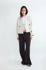 Campera estilo trench corta color beige, con solapas amplias, cierre cruzado de doble botonadura con botones oscuros y diseño holgado.