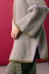 Saco oversize de tejido de punto en color beige, con mangas caídas y detalles de bordado a mano en tonos verde y lila en los bordes y costuras.