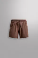 Short deportivo Zara Athleticz de color marrón, confeccionado en tejido técnico ligero y elástico con forro interior. Cuenta con cintura elástica ajustable con cordón, bolsillos frontales, bolsillo trasero con cierre de cremallera, bajo con aberturas laterales y detalle de logo estampado en la pierna.