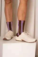 Medias de caña alta a rayas verticales marrones y lilas, con puntera y talón en lila, y logo bordado en el lateral.
