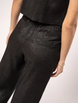 Pantalón de lino color beige, de tiro alto, pierna ancha y levemente acampanada. Tiene pinzas delanteras, elástico en la pretina trasera, cierre delantero y broche interno, bolsillos laterales y dobladillo invisible.