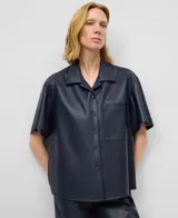Camisa de manga corta, color azul marino, confeccionada en material que simula cuero (piel no piel). Presenta cuello solapa, botonadura frontal y un bolsillo de parche en el pecho.