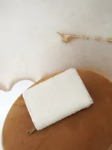 Billetera Actitud Sur de cuero con pelo vacuno en color blanco, con cierre perimetral y compartimentos internos de cuero.