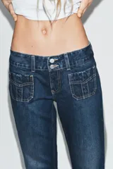Jeans de tiro bajo y corte flare, confeccionados en denim azul con lavado localizado. Presentan bolsillos de plastrón en el delantero, trabillas para cinturón y cierre frontal con cremallera y doble botón metálico.