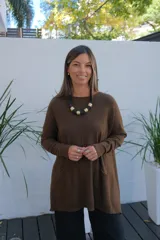 Sweater de tejido de punto en color chocolate, con corte holgado, cuello redondo y mangas largas. Presenta un diseño con bolsillos frontales integrados y terminaciones acanaladas en puños y ruedo.