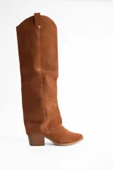 Bota de caña alta confeccionada en cuero vacuno, con diseño versátil que permite doblar la caña. Presenta un taco cuadrado de altura media y punta redondeada.