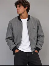 Campera bomber de paño fino en color gris con diseño de espiga (herringbone), con cierre frontal, cuello, puños y cintura elastizados en color negro, y pequeño logo bordado en el pecho.