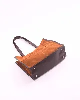 Bolso tipo shopper de gran tamaño, confeccionado en cuero gamuzado color marrón. Presenta estructura rectangular con bordes reforzados en cuero liso oscuro, doble asa de hombro y cierre mediante botón magnético.