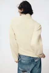 Jersey de punto liso con cuello subido, manga larga y detalle de costura vertical marcada en el frente. Presenta terminaciones en rib en puños, cuello y ruedo.