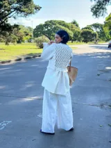 Camisa larga tipo sobrecamisa o abrigo ligero, color verde menta pálido con estampado floral en tono amarillo claro. Presenta escote en V con atado frontal mediante lazos, mangas largas con detalle fruncido y puños con flecos en tono turquesa.