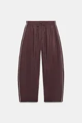 Pantalón fluido de tiro medio, confeccionado en mezcla de modal color marrón. Presenta cintura elástica con cordón ajustable, bolsillos laterales y líneas laterales en contraste de color blanco.