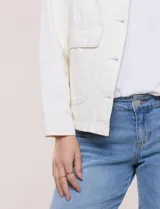 Campera de denim blanco de corte holgado con hombros caídos, cuello con solapa en contraste de color celeste, cierre frontal con botones metálicos y bolsillos delanteros con solapa.