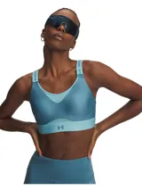 Top deportivo de alto impacto Under Armour, color azul petróleo con detalles en celeste. Presenta diseño con almohadillas moldeadas, paneles de malla para ventilación, tirantes ajustables con logo de la marca y banda elástica inferior con logo Under Armour.