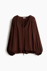 Blusa oversized de viscosa color marrón, con escote en V pronunciado, cordón para ajustar con cuentas en los extremos, frunces en los hombros, mangas globo largas con elástico en los puños y canesú fruncido en la espalda.