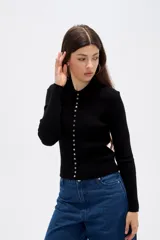Remera de manga larga ajustada al cuerpo, confeccionada en tejido acanalado de color negro. Presenta cuello tipo polo y cierre frontal con una hilera de botones pequeños.