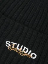 Gorro tipo beanie tejido en punto simple, color negro, con detalle de bordado frontal con la palabra STUDIO.