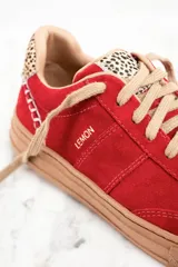 Zapatillas rojas de gamuza con cordones color beige y suela marrón. Detalle de animal print en el talón y pespuntes blancos.