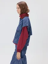 Campera de denim a rayas verticales con cuello de pana en color bordó. Presenta cierre frontal, mangas desmontables con cierre en los hombros, canesú en el pecho y bolsillos de parche cuadrados.