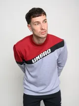 Buzo de hombre con diseño de bloques de color, combinando rojo en la parte superior de los hombros y gris melange en el cuerpo. Presenta una franja diagonal negra con el logo Umbro en blanco cruzando el pecho.