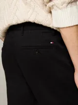 Pantalón chino negro de Tommy Hilfiger, modelo Denton, con pierna recta y confeccionado en satén de algodón elástico. Cuenta con cierre de cremallera con botón, dos bolsillos ribeteados en la cintura y dos bolsillos traseros de ojal con botón. Logo de Tommy Hilfiger bordado en la parte trasera.
