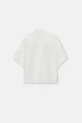 Camisa de corte fluido con cuello solapa y manga corta con dobladillo. Presenta cierre frontal con botones ocultos bajo una tapeta.