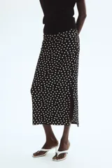 Pollera midi negra con estampado de lunares blancos, tiro alto, cintura elástica con fruncidos laterales y abertura pronunciada en un lateral.
