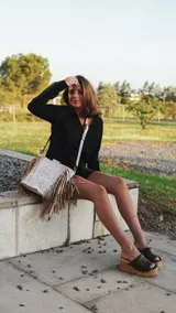 Cartera de mano tipo bolso con flecos laterales, confeccionada en cuero con acabado texturizado en tono claro. Presenta asas circulares metálicas, correa larga ajustable y extraíble, y un diseño de estilo boho.