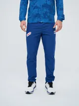 Pantalón de entrenamiento Umbro del Club Nacional de Football, modelo Grok en color azul. Presenta el escudo del club en una pierna y el logo de Umbro en la otra, con diseño cómodo y deportivo.