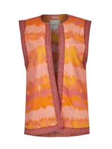 Chaleco sin mangas de estilo boho, confeccionado en algodón orgánico con estampado de ondas en tonos naranja, coral y amarillo. Presenta bordes con detalles geométricos bordados en color bordó y diseño abierto al frente.