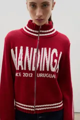 Campera tejida de algodón con cierre frontal completo, cuello alto y puños con franjas blancas. Presenta un diseño estampado con tipografía grande en el frente.