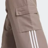 Pantalón cargo Adidas color marrón con corte holgado, cintura elástica con cordón ajustable, bolsillos laterales y bolsillos cargo. Presenta las tres rayas blancas características de la marca en los laterales.