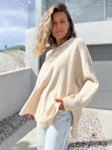 Sweater oversize de tejido de punto color crudo, con cuello redondo, manga larga con puños acanalados y detalle de costura vertical central. Presenta un diseño holgado con aberturas laterales en el ruedo.