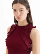 Top tejido de punto color negro, con ajuste al cuerpo, cuello redondo y volados decorativos en las sisas.