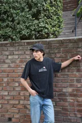 Remera de algodón 100% peinado en color gris con efecto acid wash, corte recto y mangas cortas. Presenta un estampado en la espalda de un ramo de flores acompañado por el texto "MÁS FLORES, MENOS DRAMA" y el logo de la marca.