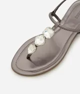 Sandalia plana color dorado, con diseño de tiras finas y aplicación de pedrería decorativa en la parte central. Cuenta con cierre de hebilla lateral ajustable.