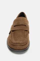 Mocasín de mujer confeccionado en serraje color marrón, con detalle de antifaz en el empeine, costuras a la vista y punta redonda. Cuenta con un pequeño tacón cuadrado.