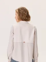 Camisa de algodón color gris claro, con cuello mao, cierre frontal de botones y mangas largas. Presenta un estampado sutil de hojas y flores, y detalles de bordado calado en los hombros.