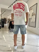 Remera oversize blanca de manga corta, con estampa en la espalda en color rojo con la inscripción 'Madness' y tipografía estilo universitario.
