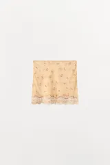 Falda mini de tiro medio confeccionada en viscosa, de color beige con delicado estampado de pequeñas flores y detalle de encaje tono sobre tono en el bajo.