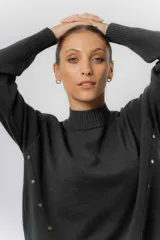 Sweater de tejido de punto color marrón, con cuello alto, corte relajado y terminaciones en rib en puños y cintura. Presenta una hilera de botones metálicos decorativos en uno de los laterales.